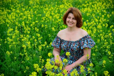 Çiçekli çayırda oturan güzel orta yaşlı kadın