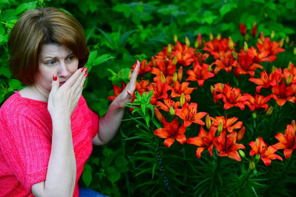 Frau mit allergischem Schnupfen in der Nähe von Lilien in der Natur — Stockfoto