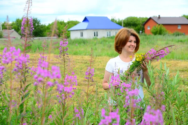 Femme avec bouquet de fleurs sauvages sur le fond du village — Photo