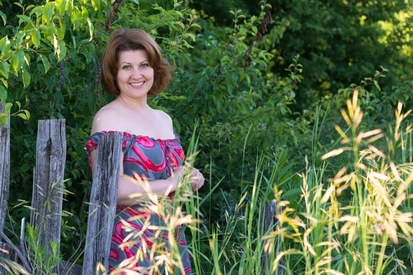 Woman in dress with open shoulders stands near the fence — Stock Photo, Image