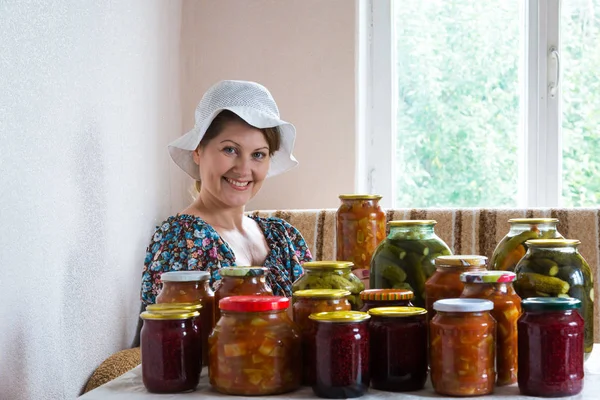 Жінка сидить за столом з домашніми консервованими овочами і варенням — стокове фото
