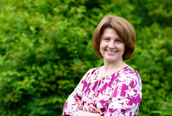 Portret van lachende vrouw tegen een achtergrond van groen gebladerte — Stockfoto