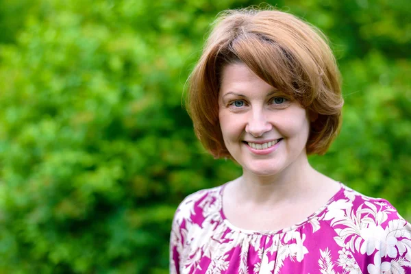 Portret van lachende vrouw tegen een achtergrond van groen gebladerte — Stockfoto