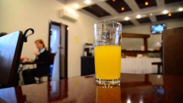 Un vaso de jugo de naranja sobre una mesa en un café — Vídeos de Stock