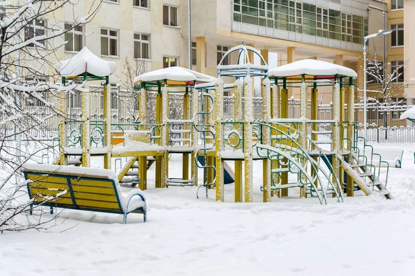 children's play complex and bench in snow around the building