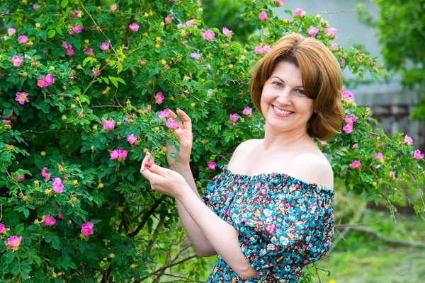 Smiling woman standing near blossoming dog rose — Stock Photo, Image