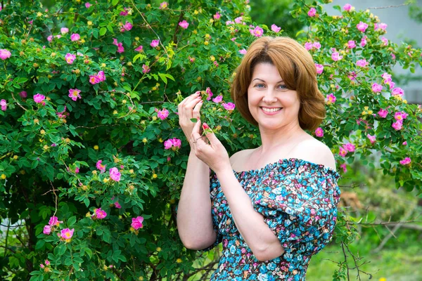 Smiling woman standing near blossoming dog rose — Stock Photo, Image