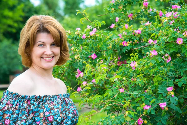Porträtt av vacker kvinna på bakgrund av en blommande vilda ros — Stockfoto