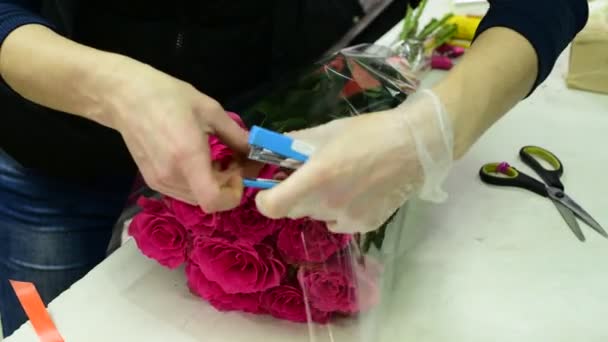 Флорист обернет букет роз в прозрачную упаковку — стоковое видео