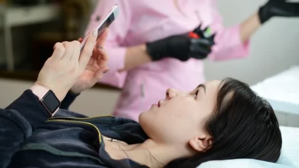 Chica joven se encuentra en el sofá y el uso de teléfono inteligente antes de un procedimiento médico — Vídeo de stock