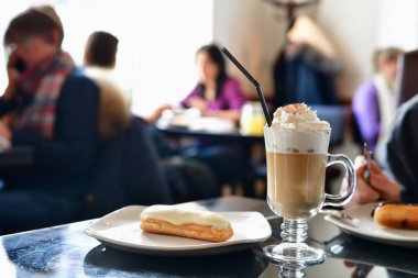 coffee with whipped cream and eclair on table in a cafe clipart