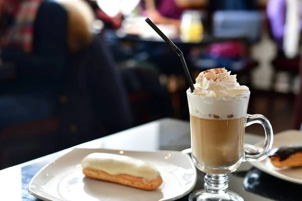 Café con crema batida y eclair en la mesa en un café —  Fotos de Stock