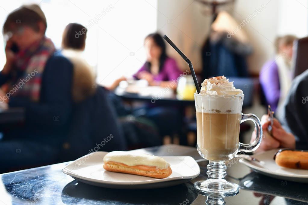 coffee with whipped cream and eclair on table in a cafe