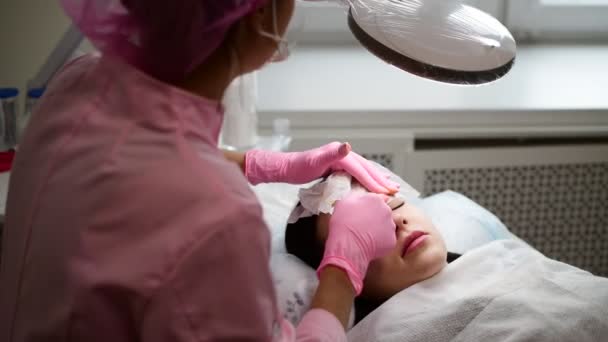 Косметолог видаляє залишки фарби за допомогою чистки тканини з брови дівчинки — стокове відео