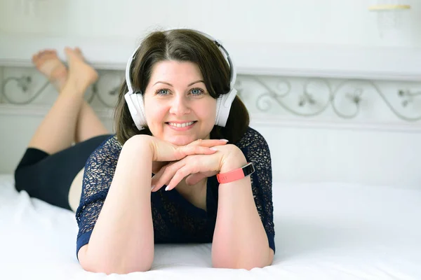 woman listens to music on headphones and lies on bed
