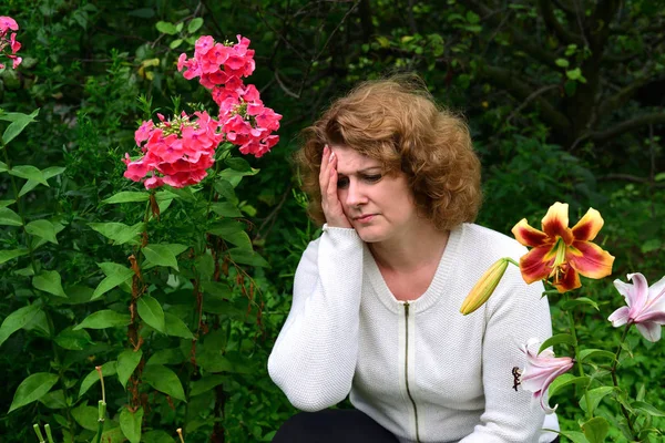 Γυναίκα με πονοκέφαλο στο φόντο των λουλουδιών — Φωτογραφία Αρχείου