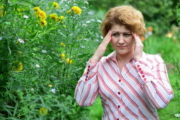 Mujer con dolor de cabeza cerca de las flores amarillas —  Fotos de Stock