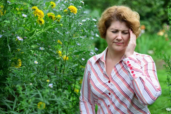 Donna con mal di testa vicino ai fiori gialli — Foto Stock