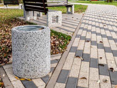 Çöp tenekesi ahşap bankın yanında.