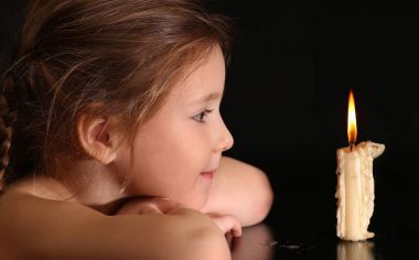 Portrait of a Girl 4-5-6 years, looking at the burning candle isolated on black background. clipart