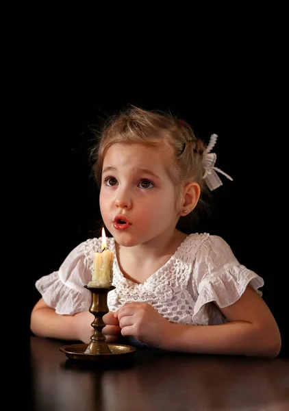 Portret van een meisje 4-5-6 jaar, kijken naar de brandende kaars geïsoleerd op zwarte achtergrond. — Stockfoto