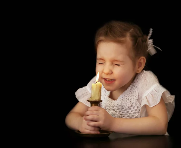 Retrato de uma menina 4-5-6 anos, olhando para a vela acesa isolada no fundo preto . — Fotografia de Stock