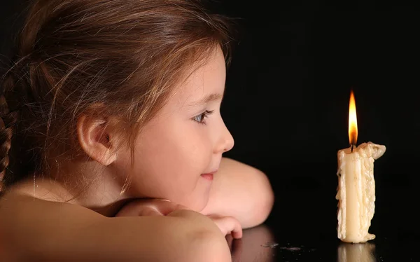 Portret van een meisje 4-5-6 jaar, kijken naar de brandende kaars geïsoleerd op zwarte achtergrond. — Stockfoto