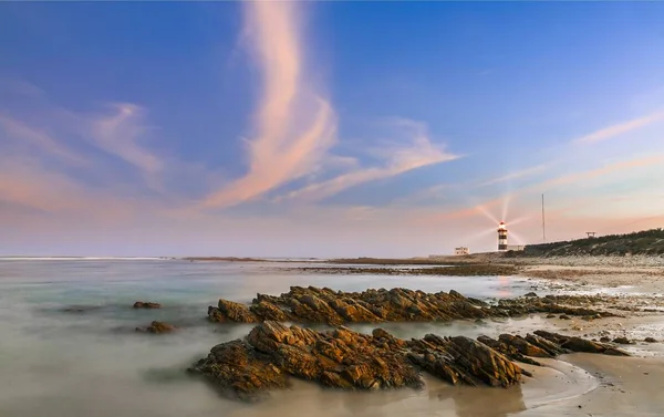 Lighthouse at dusk with rocks in the foreground — Stock Photo, Image
