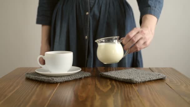 Mujer vertiendo leche en una taza de café — Vídeos de Stock