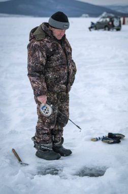 Baykal Gölü, Sibirya, Rusya - 05 Mart 2020: Buz balıkçılığı. Mart 'ta Baykal Gölü' nde bir balıkçı çadırların ve arabaların yanında balık tutuyor. Baykal Gölü, Sibirya, Rusya