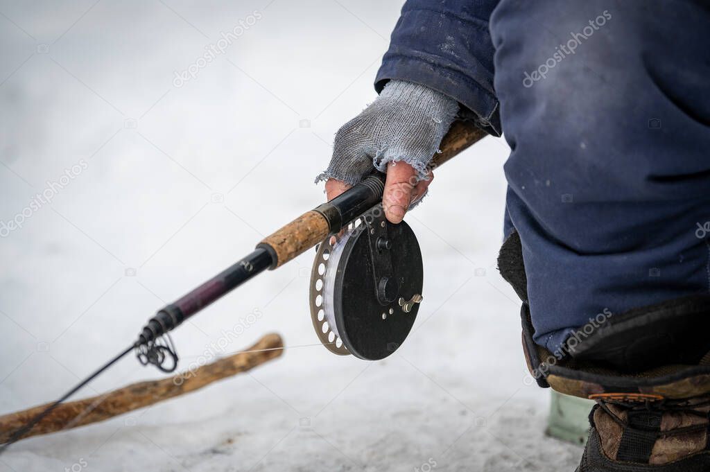 Baikal lake, Siberia, Russia - March 05, 2020 : Winter ice fishing. A fisherman is fishing on spinings near tents and cars on Lake Baikal on a March day. Baikal lake, Siberia, Russia