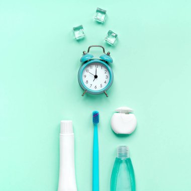 Diş hijyeni, ağız bakımı ürünleri ve yeşil naneli arkaplan üzerindeki alarm saati fotokopi alanı ile. Boş diş macunu tüpü, diş ipi ve diş fırçası. Düz konum, üst görünüm bileşimi, model