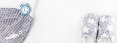 Uyku. Kabarık terlik, hap lar ve beyaz arka plan üzerinde izole mavi çalar saat ile şişe. Yaratıcı kavramsal üst görünüm düz minimal tarzı yatıyordu. Dinlenme, iyi geceler, uykusuzluk, rahatlama, yorgun kavramı