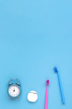 Diş hijyeni ve ağız bakımı ürünleri ve mavi arka planda kopya alanı olan alarm saati. İki aile diş fırçası. Düz konum, üst görünüm kompozisyon, model. Sabah rutini konsepti