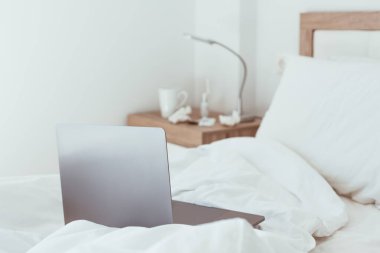 Ev karantinasında çalışmak kendini tecrit etme kavramı. Dizüstü bilgisayar yapılmamış yatakta. Rahat ve uzaktan kumandalı ev ofisi. Günışığı ve minimalist tasarımı olan modern daireler. Salgında güvende ol..