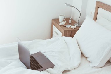 Ev karantinasında çalışmak kendini tecrit etme kavramı. Dizüstü bilgisayar yapılmamış yatakta. Rahat ve uzaktan kumandalı ev ofisi. Günışığı ve minimalist tasarımı olan modern daireler. Salgında güvende ol..