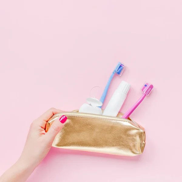 牙齿卫生和口腔卫生产品在黄金旅行化妆品钱包上的粉刷粉红的背景与副本空间在妇女手修指甲 平面布局 顶视图构图 — 图库照片