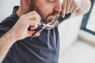 Karantina sırasında kişisel bakım. Yetişkin, yakışıklı, beyaz bir adam evde bıyık ve sakal kesiyor. Coronavirus salgını ve insanların kendini kapatması, evde kalma kavramı