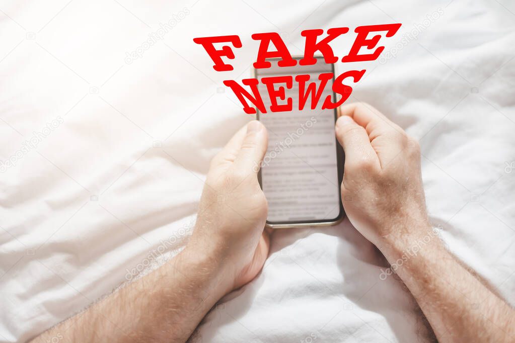 Fake news infodemics during Covid-19 pandemic concept. Man hands holding mobile phone reading global news or social net at home. Reading last news update in lockdown. Red text fake news on foreground