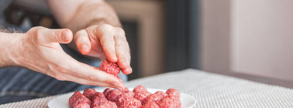 Man hands preparing meatballs with raw mincemeat. Lifestyle close up composition with natural light. Homemade cooking during lockdown, stay home housekeeping sharing concept. Side view with copy space