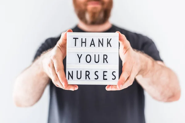 Nurse day concept. Man hands holding lightbox with text Thank your nurses thanking doctors, nurses and medical staff working in hospitals during coronavirus COVID-19 pandemics