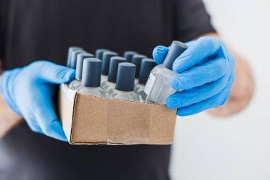 Coronavirus COVID-19 salgını sırasında lateks eldiven takan ve koruyucu maske takan adamın ellerinde el hijyen jeli şişeleri var. Sağlık ve güvenlik önlemleri