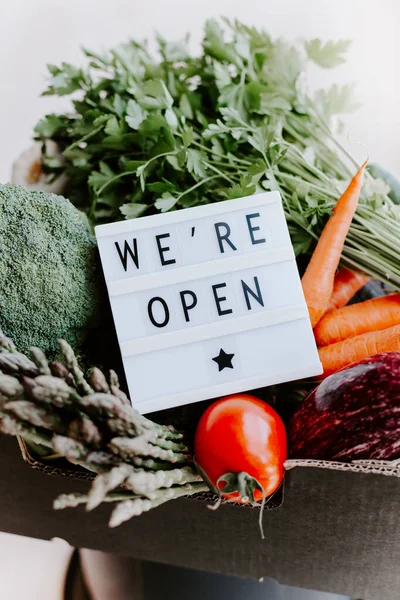 End of quarantine lockdown. Lightbox with greeting text message We\'re open and Fresh greens and vegetables box. Welcoming grocery shop clients after coronavirus Covid-19 pandemic outbreak
