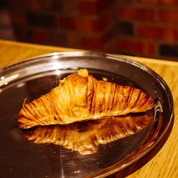 Leckeres Croissant auf reflektierendem Teller — Stockfoto