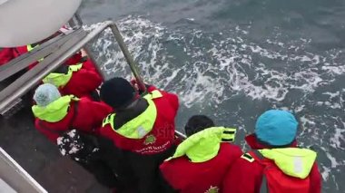 Husavik, İzlanda, 17 Ağustos 2017: Küçük bir sürat teknesinde balina turu izleyen turistler. Hepsi eşleşen sıcak tulumlar giyiyor..