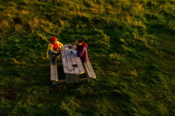 Dos mujeres turistas sentadas a la mesa en Islandia en el atardecer tim —  Fotos de Stock