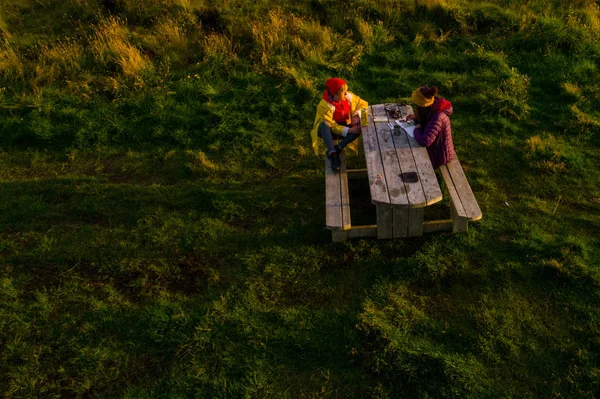 Dos mujeres turistas sentadas a la mesa en Islandia en el atardecer tim —  Fotos de Stock