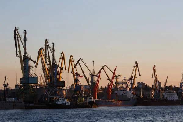 BERDYANSK - UCRANIA, 02 DE SEPTIEMBRE DE 2016: Muchas grúas grandes silueta en el puerto a la luz dorada del amanecer reflejada en el agua — Foto de Stock