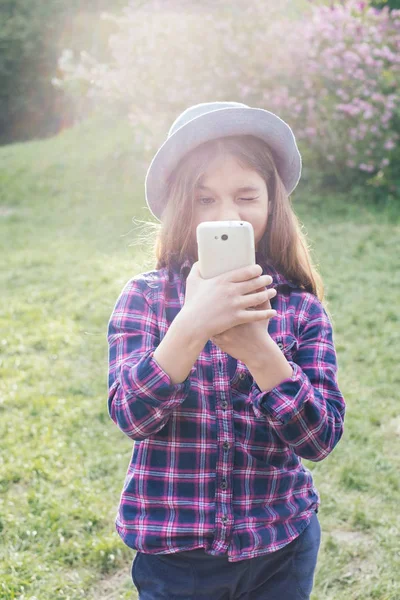 Urocza tweenie pre-teen dziewczyna brunetka dziecko z jej smartphone w parku wiosny — Zdjęcie stockowe