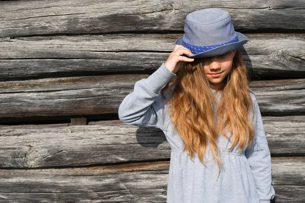 Радостная девочка-подросток с длинными волосами в повседневной одежде и синей шляпой, позирующей у деревянной стены. Активный образ жизни. Мода молодежи — стоковое фото